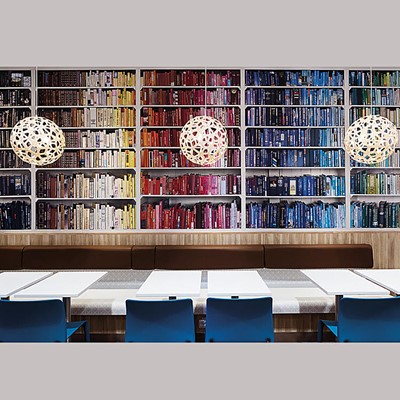 Interior image showing tables and a wall full of colourful books. Photo. 